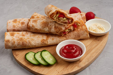 Shawarma, fresh roll of pita, chicken, vegetables. Traditional Middle Eastern snack on a wooden board