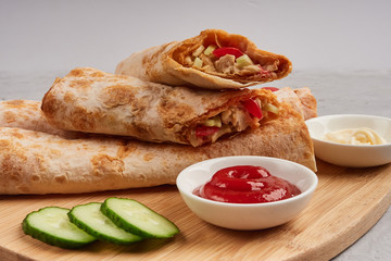 Shawarma, fresh roll of pita, chicken, vegetables. Traditional Middle Eastern snack on a wooden board
