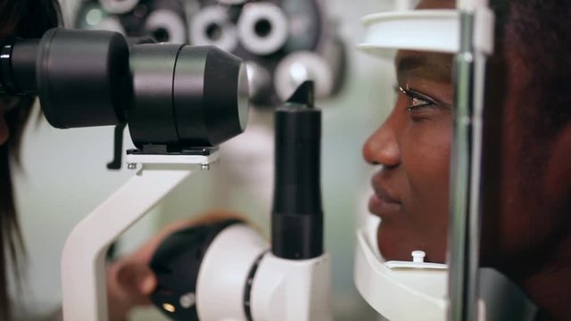side view of an afro woman in an optometry cabinet correcting her eyesight	with a ophthalmometer