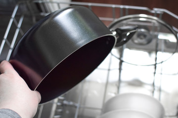 Clean bowls and pans are in the dishwasher. The man pulls out a clean pot. Hand close-up. Selective focus