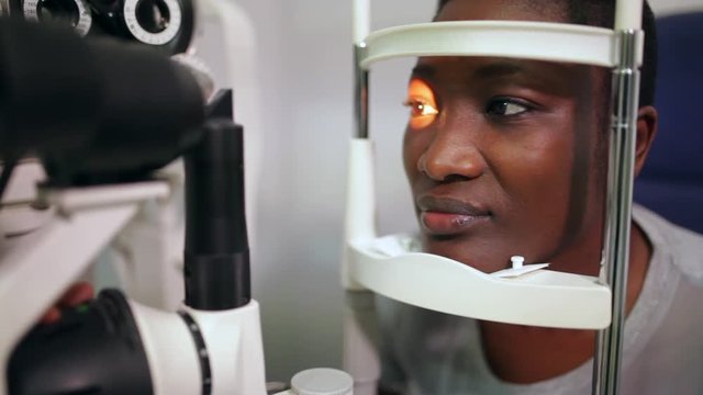 side view of an afro woman in an optometry cabinet correcting her eyesight	with a ophthalmometer