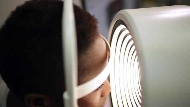side view of an afro woman in an optometry cabinet correcting her eyesight with a ophthalmometer