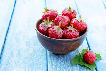 red strawberry lies on green leaves against the background of blue old boards.