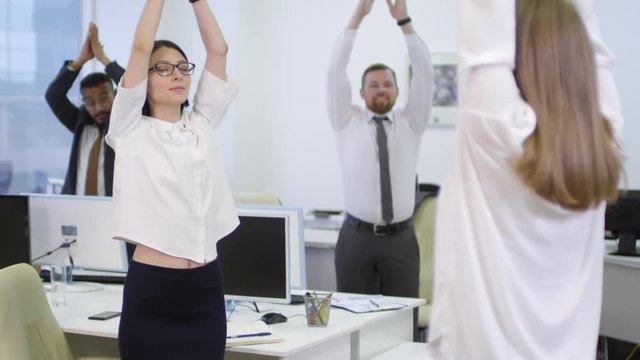 Panning of female manager encouraging team of office workers doing meditating exercises together at their workplaces