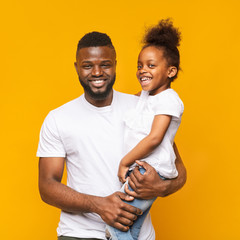 Cheerful african dad holding his cute daughter on hands