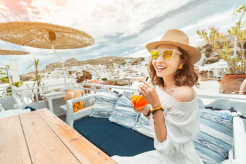 Happy asian woman enjoying aperol spritz cocktail in a greek cafe. Beverage and refreshment concept