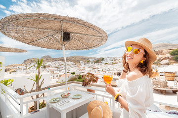 Happy asian woman enjoying aperol spritz cocktail in a greek cafe. Beverage and refreshment concept
