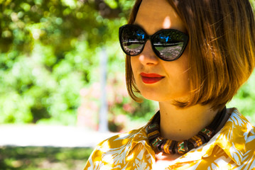 Beautiful girl in sun glasses and ethnic necklace in summer park.