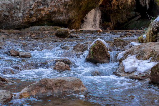 Cold mountain river flows between stones with snow and ice, selective focus, waterfall in the background, Karachay-Cherkess Republic