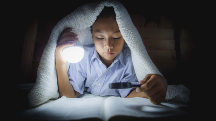 Christian boy reading and searching bible under the covers at night. focus at face.
