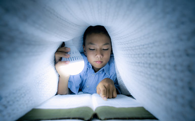 Christian boy reading bible under the covers at night. focus at face.