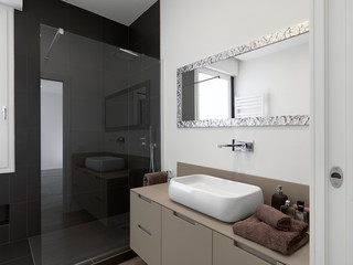 foreground the counter top washbsin  on the wooden sink cabinet in the modern bathroom on the background the masonry shower cabin