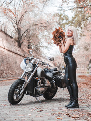 Beautiful biker woman posing with autumn leaves on the road.