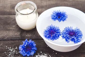 Obraz na płótnie Canvas blue cornflowers lie in the water in a white bowl near a burning candle on the background of old boards.