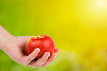 Healthy food concept. Woman's hand holding red appl against green natural background.