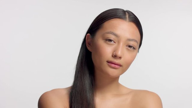 mixed race asian model in studio beauty shoot Model poses to a camera, straight hair combed to right side. Ideal skni and no makeup makeup Head and shoulders crop