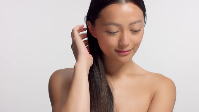 mixed race asian model in studio beauty shoot. Head and shoulders crop model touches her hair and watching to the camera