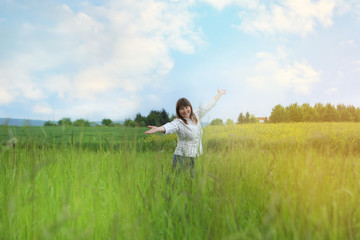 a woman in the field is standing enjoying nature, spreading her arms apart, uniting with nature