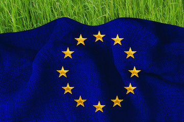 The blue flag of the European Union on the dense burlap lies on the lush green grass