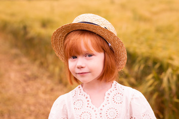 Portrait of beautiful red-haired girl in the gold field. Summer time