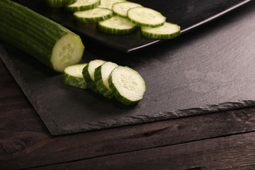 Fresh sliced cucumbers on black cutting board and wood rustic background. Flat lay pattern of green cucumbers on table