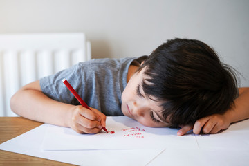 Emotional portrait of child writing a letter to his mother, Preschool kid using red colour writing...