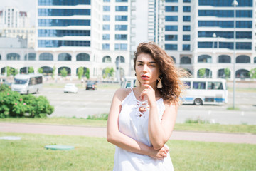 Portrait of a beautiful elegant woman in light white dress standing in the summer park.