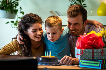 Happy family celebrating a birthday together at home. Young parents with son blowing candles on...