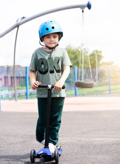 Fototapeta na wymiar Portrait boy learning to ride a scooter in playground in sunny day summer, Prortrait Child in safety helmet riding a roller, Kid playing outdoors, Active leisure and outdoor sport for children.