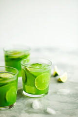 Homemade trendy iced matcha green tea or lemonade with cucumber and lime in a glass on light gray background with copy space for text.Healthy cold vegan beverage for hot summer day.Super food drink