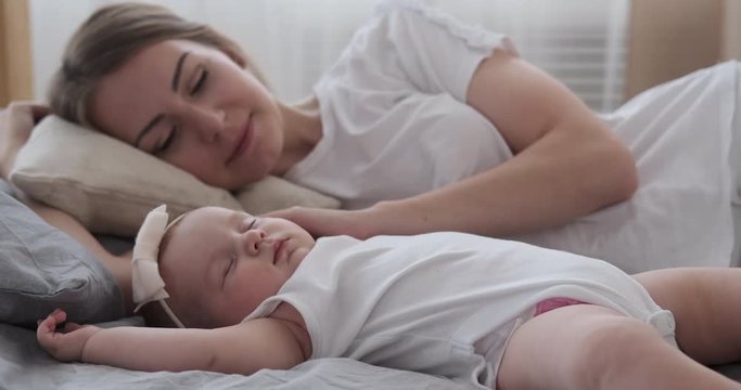 Woman stroking her cute baby daughter sleeping on bed