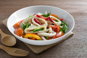 spicy squid ring salad in a ceramic plate on wooden table, close up. homemade style food concept.