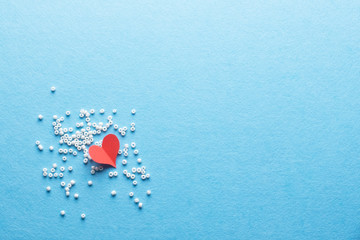 Red paper heart on white tiny beads on blue background. Love concept.