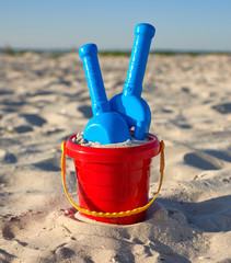 red plastic bucket and blue rake, shovel on the sand