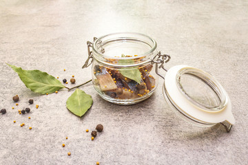 Slices of herring with spices in a glass jar.