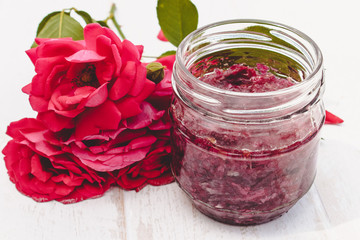 Jar of jam of rose petals on a wooden table with flowers of roses. Flower confiture. Healthy food.