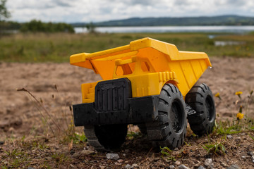 A child's yellow dump truck abandoned on the ground by a lake