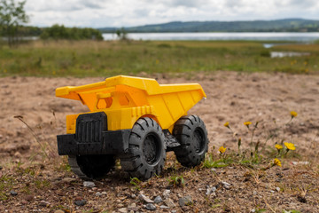 A child's yellow dump truck abandoned on the ground by a lake, taken at ground level