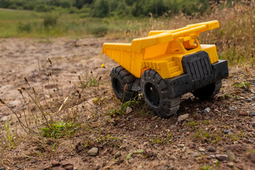 A child's yellow dump truck abandoned on the ground by a lake, three quarter view