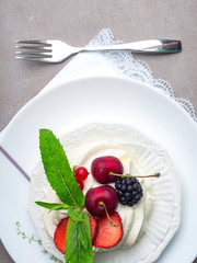 Pavlova meringue cake with fresh berries, mint on white plate with fork