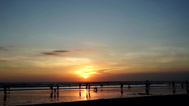 Ocean beach at sunset. Moving people (young and children and old), sand bay. Orange and blue sky with clouds. Timelapse