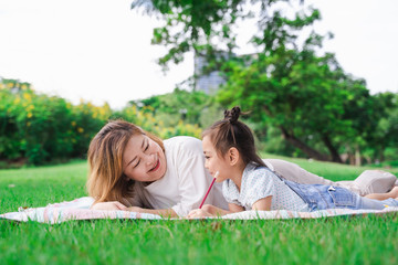 Asian grandmother and granddaughter laying on the green glass field outdoor, family enjoying picnic together in summer day