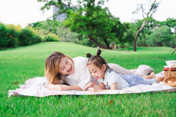 Asian grandmother and granddaughter laying on the green glass field outdoor, family enjoying picnic together in summer day