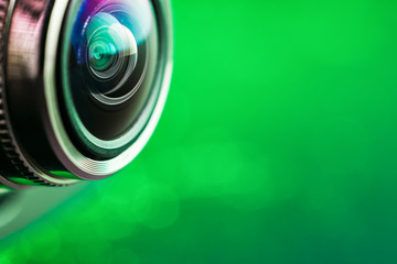  Camera lens and green backlight. Side view of the lens of camera on green background. Camera Lens Close Up. Optics