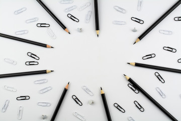 Black pencils and paper clips, white buttons and paper clips lie on a white background.