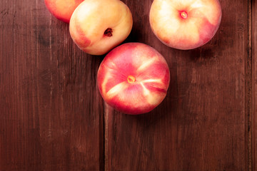 An overhead closeup photo of vibrant organic flat saturn peaches on a dark rustic wooden background...
