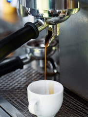 Close up details of brewing machinery pouring and preparing fresh espresso in small classic white ceramic cup. Cozy craft city cafe shop details
