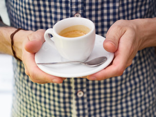 Close up of barista man hands serving freshly brewed cappucino coffee while standing in coffee shop. Focus on male hands holding a big white ceramic cup of coffee with copyspace