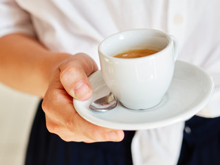 Close up of barista man hands serving freshly brewed cappucino coffee while standing in coffee shop. Focus on male hands holding a big white ceramic cup of coffee with copyspace