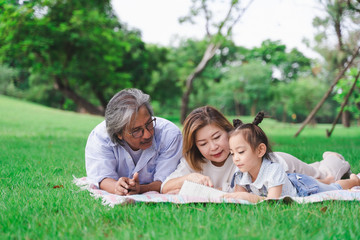 Asian grandparents and granddaughter are lying on the grass field outdoor, asian family concept